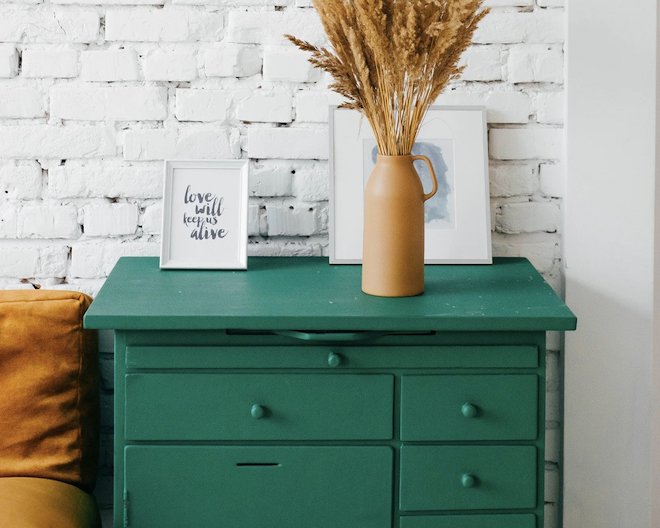 a green set of drawers with a mug of flowers on top